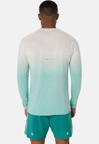 Långärmad träningsskjorta i gradient från vitt till teal, med ett strukturerat mönster och kontrasterande sömmar; i kombination med teal shorts med prickdetaljer.