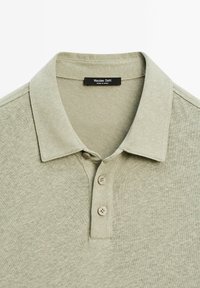 Polo shirt verde pallido realizzato in tessuto teksturato. Presenta un colletto classico, una chiusura a tre bottoni e dettagli di cucitura sottili.