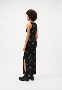 Rochie maxi neagră, fără mâneci, cu un design tricotat texturat, broderie florală și fante laterale. Asortată cu botine platformă negre, cu talpă groasă.