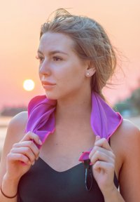 Purple cooling towel with pink accents draped around shoulders, held by individual. Textured fabric, lightweight, suitable for outdoor use.