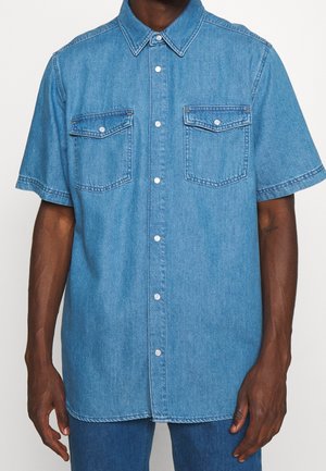 Denimhemd in hellblau, mit kurzen Ärmeln, klassischem Kragen, zwei Brusttaschen und einer Frontknopfleiste mit silbernen Akzenten. Glatte Textur.