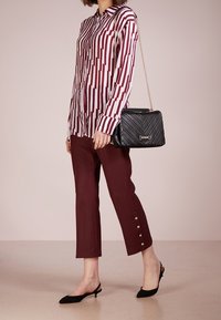 Pasiasta burgundowa i biała koszula z kołnierzykiem i zapinanymi mankietami, w zestawieniu z burgundowymi spodniami z guzikami. Czarna pikowana torebka i szpilki.