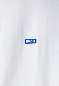 White T-shirt made of cotton, featuring a blue rectangular embroidered logo that reads "HUGO," positioned on the left chest area.