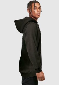 Sudadera negra hecha de una tela suave, con un bolsillo canguro y puños acanalados. Presenta una capucha con cordón y un diseño gráfico en la parte posterior.