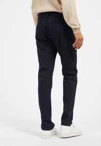 Chinos blu navy con vestibilità dritta, realizzati in cotone, dotati di tasche posteriori e una texture liscia. Abbinati a sneaker bianche.