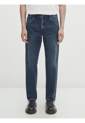 Donkerblauwe denim jeans met een rechte pasvorm, vijfzakken ontwerp, subtiele vervaging en ton-sur-ton stiksels, gecombineerd met zwarte veterschoenen.