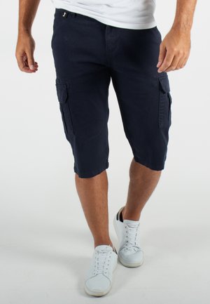 Shorts cargo bleu marine en coton, dotés de plusieurs poches latérales, d'une coupe au genou et d'un fit décontracté. Portés avec des baskets blanches.