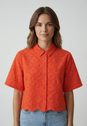 Mujer con una camisa de botones de manga corta color naranja brillante con un patrón de ojales y dobladillo en forma de ondas, combinada con jeans azul claro.