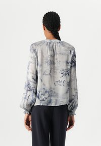 Bluză cu mânecă lungă, de culoare albastră deschisă, cu print floral, având mansete elastice și croială boxy, realizată dintr-un material ușor, texturat.