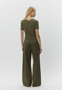 Alyvuogių žalumo, prigludęs trumpomis rankovėmis marškinėliai, derinami su plačiomis, aukštu liemeniu kelnėmis. Minkšta tekstūra ir minimalistiškas dizainas su dviem užpakalinėmis kišenėmis.