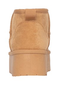 Botín de ante beige con superficie texturizada, suela gruesa y tirador trasero. Diseño elegante con punta redondeada y detalles mínimos.