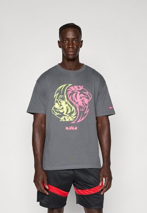 Pelēka T-kreklu ar divām lauvu grafikām rozā un dzeltenā krāsā, ar apaļu kakla dizainu un īsām piedurknēm. Nike logo kreisajā piedurknē.