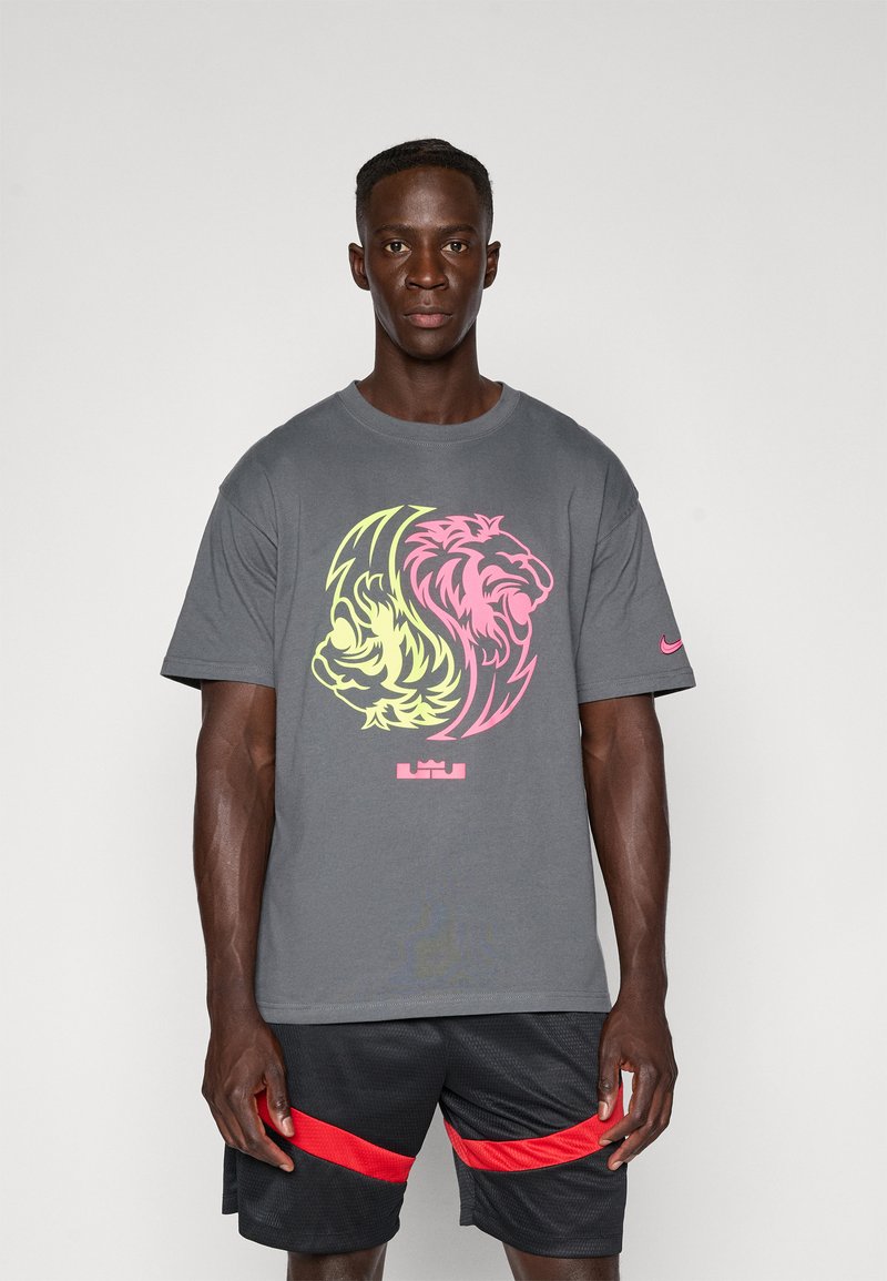 Grå T-shirt med et dobbelt løvнинг grafisk design i pink og gul, rundhalset og med korte ærmer. Nike-logo på venstre ærme.