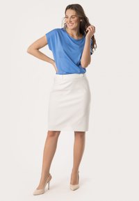 Blauwe blouse met korte mouwen gecombineerd met een witte kokerrok en naakte hoge hakken. Glad materiaal met een relaxte pasvorm, die de silhouet accentueert.
