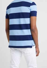 Polo de manga corta con rayas horizontales en azul marino y celeste, hecho de algodón, con aberturas laterales y dobladillo recto.