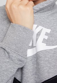 Gray sweatshirt with a high collar and white logo. Features soft texture and ribbed cuffs. Includes a black accent at the hem.