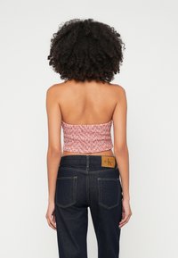Röd och vit mönstrad kort tube top med smockad design, i kombination med mörkblå denimjeans med läderetikett och bakfickor.