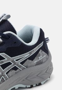 Zapatilla deportiva en azul marino y azul claro con parte superior de malla, suela de goma y prominente logo de Asics; presenta patrones texturizados y un diseño que brinda soporte.