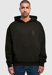 Felpa nera con cappuccio e tasca frontale, caratterizzata da una piccola grafica di una mano e un cuore in bianco e rosso sulla parte sinistra del petto.