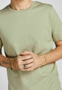 Vaaleanvihreä lyhythihainen t-paita, joka on valmistettu pehmeästä kankaasta. Ominaisuuksiin kuuluu klassinen pyöreä kaula-aukko ja sileä pinta, joka on yhdistetty monimutkaisiin koru yksityiskohtiin.