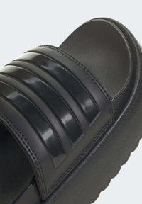 Sort slide sandal med tre glansfulde vandrette striber, tekstureret fodseng og en tyk, bølget sål for forbedret greb og komfort.