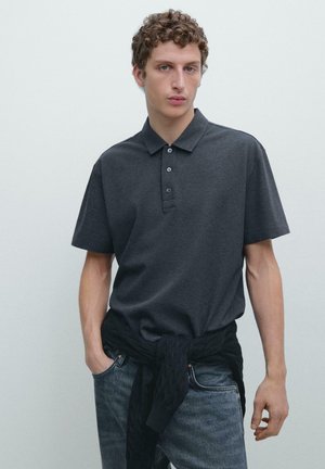 Polo grigio scuro con colletto classico, patta con tre bottoni, maniche corte e vestibilità comoda, abbinata a jeans scuri e una cintura lavorata a maglia.