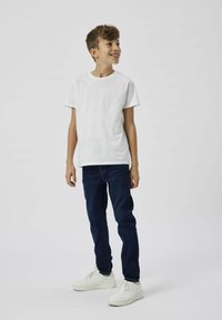 Camiseta de algod�ón blanca con cuello redondo, combinada con unos jeans de denim azul oscuro y zapatillas blancas. Ajuste sencillo y casual sin patrones visibles.