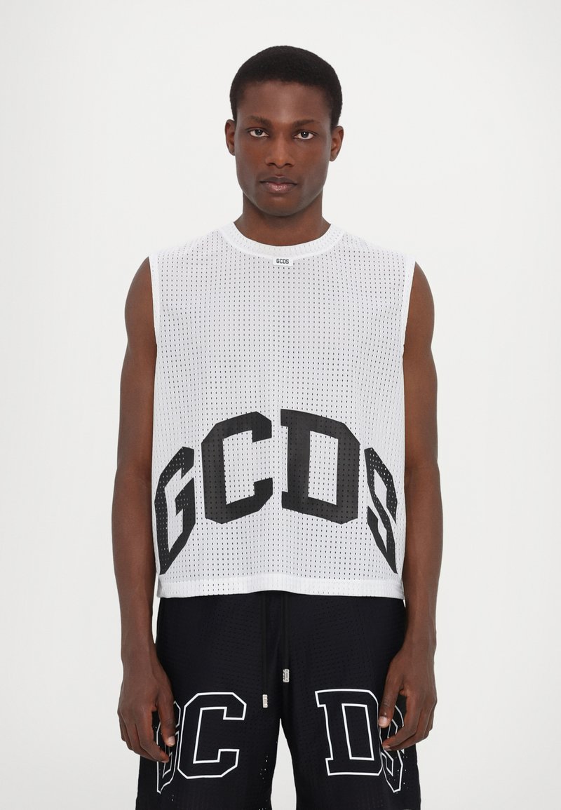 Top senza maniche in rete bianca con grande logo nero "GCDS". Collo rotondo e vestibilità ampia. Indossato con pantaloni corti neri con dettagli bianchi.