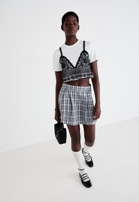 Camiseta blanca cortada con una bralette negra de encaje encima, combinada con una falda plisada a cuadros, un bolso negro y calcetas blancas hasta la rodilla con zapatos negros.