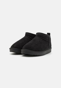 Botines de ante negro con punta redondeada, panel lateral elástico y suela de goma texturizada con un ligero tacón.