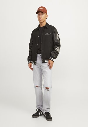 Black varsity jacket with leather sleeves, white stripes on cuffs, paired with light denim jeans featuring distressed knees and black sneakers.