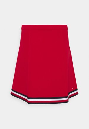 Červená sukně do áčka s černým, bílým a červeným pruhovaným lemem na spodním okraji, s úzkým pasem a malým logem na boku.