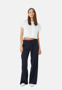 Witte cropped T-shirt met reliëftekst "GOOD VIBE 1998," gecombineerd met marineblauwe wijde broek met een rood-witte gestreepte tailleband.
