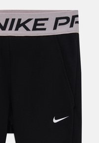 Juodos sportinės kelnės su pilku juosmeniu, kuriame užrašyta "NIKE PRO" juodu tekstu. Įvairiuose šonuose yra kišenės ir mažas baltas "Nike" logotipas.