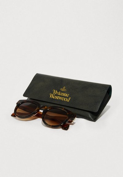 Rjave tortoiseshell sončna očala s kroglastimi okvirji, postavljena ob črni usnjeni etui, na katerem je v zlatem tisku napis "Vivienne Westwood".