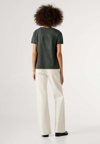 Tumehallist puuvillast T-särk lühikeste varrukatega ja tekstuurse tagapaneeli disainiga, koos valgete laia säärega teksade ja mustade kingadega.