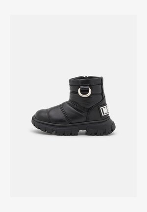 Bota de tornozelo preta feita de couro suave com bico arredondado, tira lateral com um anel de metal e sola de borracha rugosa texturizada.