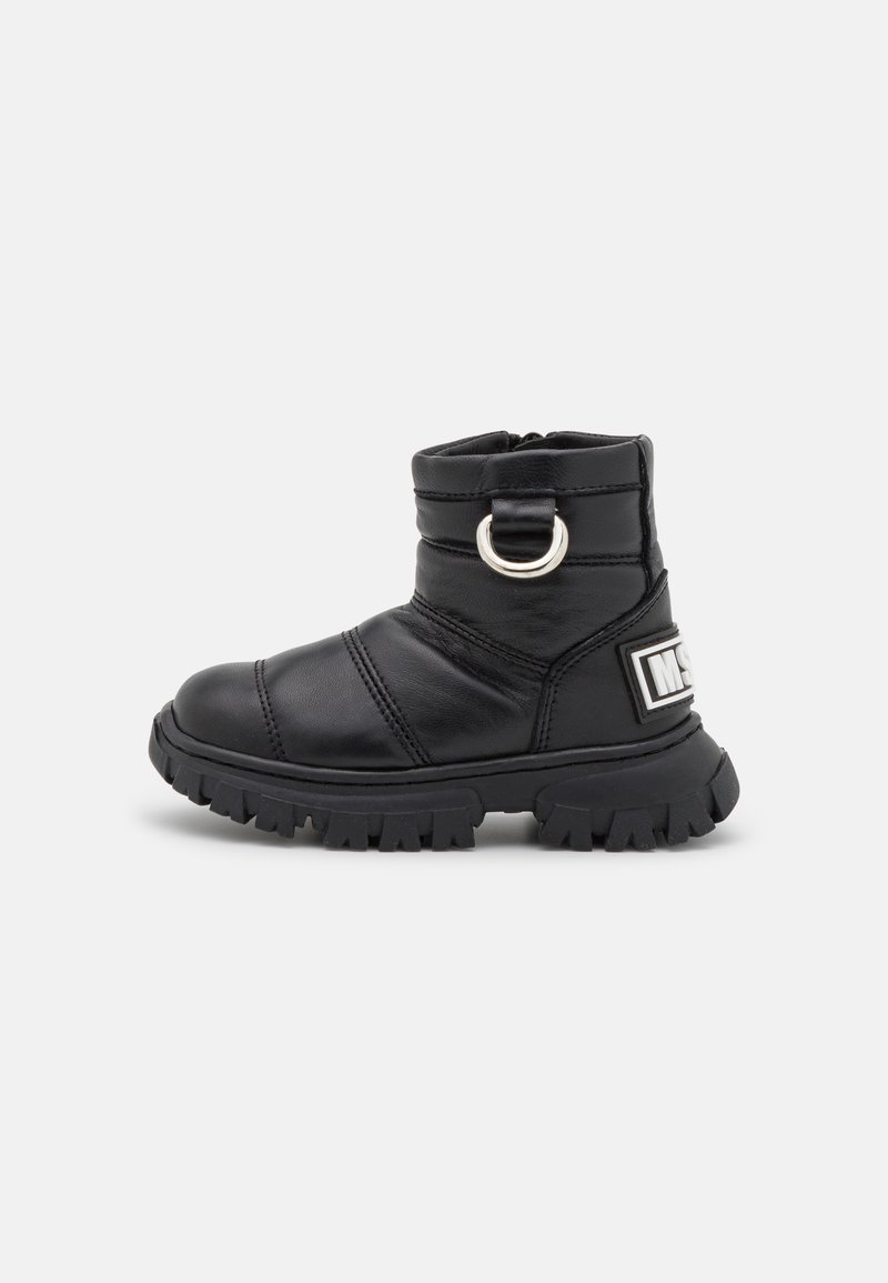 Bota de tornozelo preta feita de couro suave com bico arredondado, tira lateral com um anel de metal e sola de borracha rugosa texturizada.