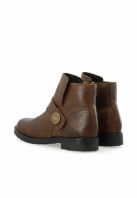 Bruna läderstövlar vid ankeln med rund tå, sidostropp och dekorativ knappdetalj. Texturerad gummisula, elegant midjhög design.