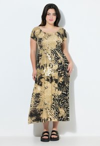 Robe maxi en imprimé animal doré et noir. Elle présente un corsage smocké, des manches courtes et une silhouette fluide. Associée à des sandales noires épaisses.