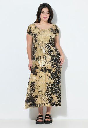 Maxikleid in einem goldenen und schwarzen Tierdruck. Es hat ein gerafftes Mieder, kurze Ärmel und eine fließende Silhouette. Kombiniert mit klobigen schwarzen Sandalen.