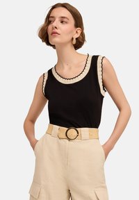 Czarny, bezrękawnikowy top z falbaniastym, kremowym dekoltem i wykończeniami rękawów, zestawiony z beżowymi, wysokim stanem spodniami z szerokim paskiem z okrągłą klamrą.