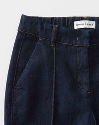 Pantalons en denim bleu foncé avec des coutures orange visibles. Dispose d'une ceinture et d'une poche latérale, étiquetés "OPUS PANTS" à l'intérieur.
