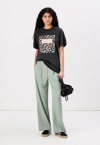 Black oversized t-shirt with leopard print design and "L'amour" text. Paired with light green wide-leg trousers and a black patterned bag.