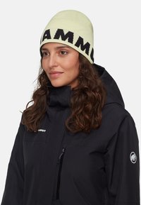 Berretto di maglia color verde chiaro con lettering nero audace. Indossato con una giacca nera dotata di tasca con zip e toppa con logo.