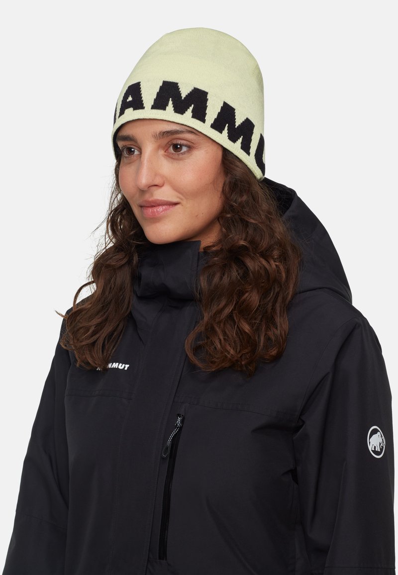 Berretto di maglia color verde chiaro con lettering nero audace. Indossato con una giacca nera dotata di tasca con zip e toppa con logo.