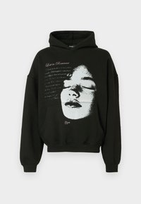 Μαύρο φούτερ με κουκούλα από βαμβάκι με χαλαρή εφαρμογή· διαθέτει λευκό σχέδιο προσώπου και το κείμενο «Lost in Romance» τυπωμένο με ροζ χρώμα.