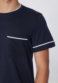 T-shirt en coton bleu marine avec un col rond, des manches courtes avec une finition blanche, et une poche sur la poitrine gauche avec une ligne d'accent blanc.