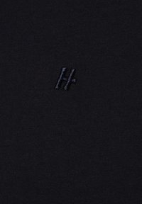 Czarny materiał o gładkiej teksturze z małym, ciemnoniebieskim haftowanym logo w kształcie nałożonych liter "H" i "+".