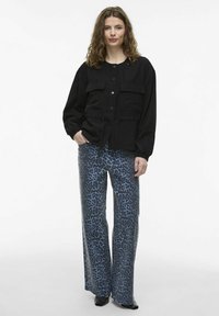 Čierna látková bunda s predným zapínaním na gombíky, dvoma náprsníkovými vreckami a sťahovacím pásom; modré nohavice s leopardím vzorom a širokými nohavicami; čierne kotníkové topánky.